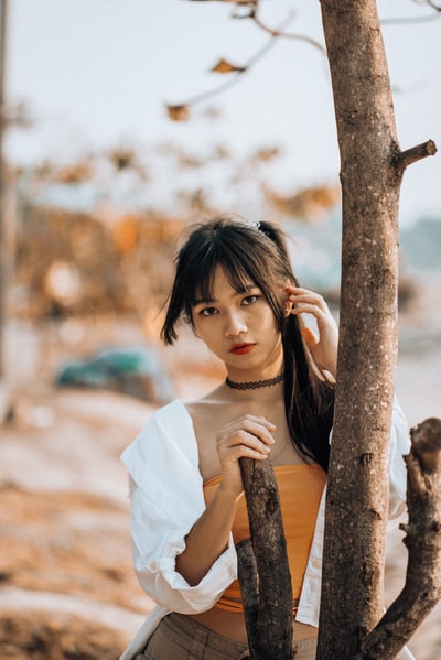 白天，一个穿着白色衣服的女人靠在棕色的树干上